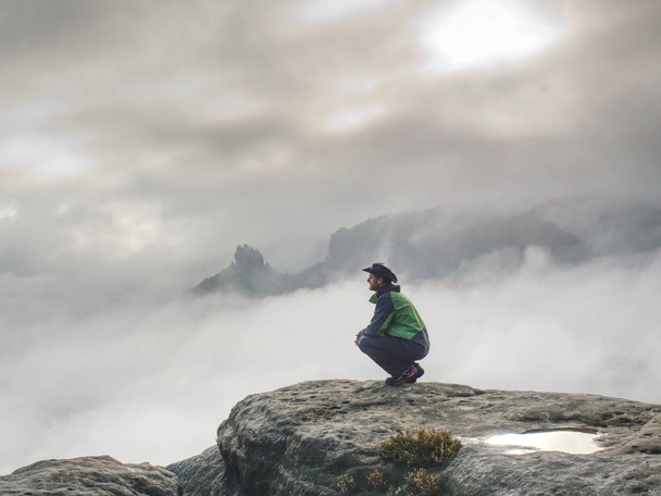 Hombre fuerte en chaqueta verde y sombrero de vaquero relajarse en el acantilado agudo
 - Foto, imagen