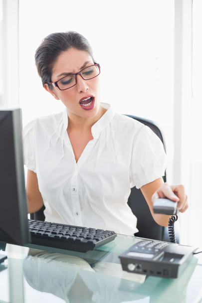Angry businesswoman sitting at her desk hanging up the phone - Photo, Image