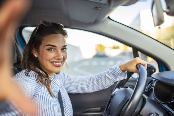 Smiling young woman taking selfie picture with camera in car. Holidays and tourism concept - smiling teenage girl taking selfie picture in car. Beautiful young woman in car, taking selfie - Фото, зображення