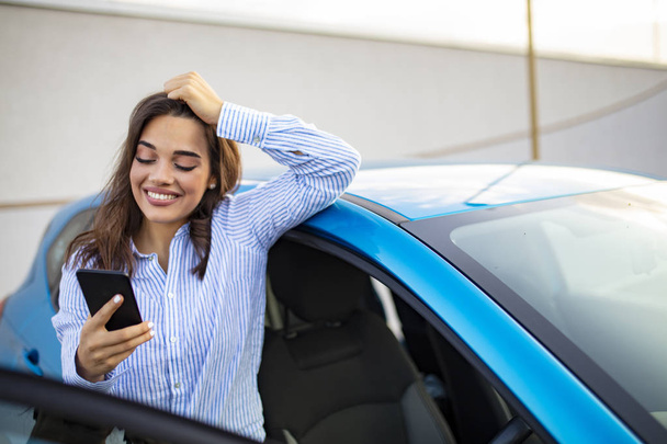 Road trip, technology and communication concept - happy young woman calling on smartphone near car. Business Woman Uses Smartphone While Leaning on Her Car - Zdjęcie, obraz