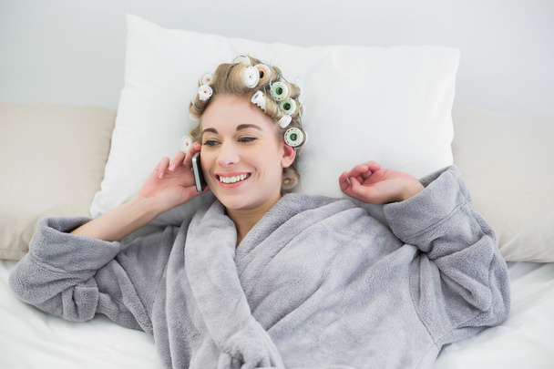 Delighted relaxed blonde woman in hair curlers making a phone call - Foto, Bild
