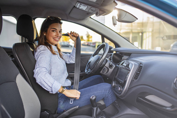 Young girl is fastening her seat belt. Photo of a business woman sitting in a car putting on her seat belt.  Woman fastening seat belt in the car, safety concept  - Zdjęcie, obraz