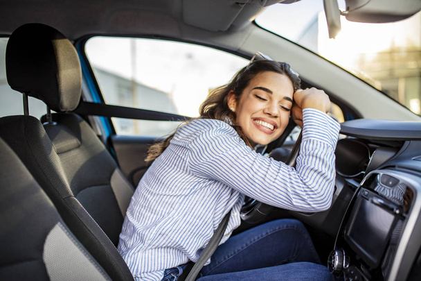 Young and cheerful woman enjoying new car hugging steering wheel sitting inside. Woman driving a new car. Woman Driver Portrait at Car - Photo, image