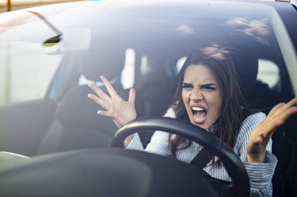 Closeup portrait, angry young sitting woman pissed off by drivers in front of her and gesturing with hands. Road rage traffic jam concept. Woman is driving her car very aggressive and gives gesture with his fist - Fotoğraf, Görsel