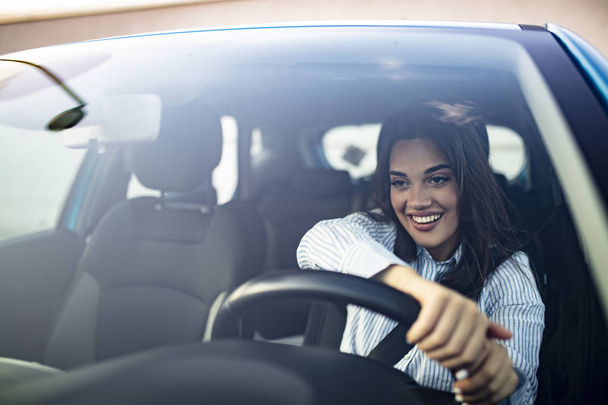 Beautiful young happy smiling woman driving her new car at sunset. Young woman driving a car in the city. Portrait of a beautiful woman in a car, looking out of the window and smiling.  - Fotoğraf, Görsel
