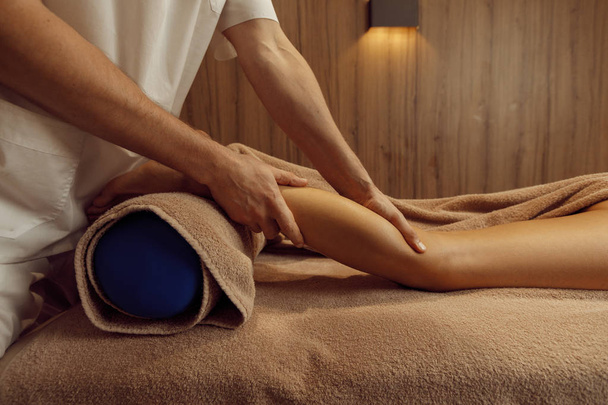 Masseur masculin étirant les jambes à la jeune femme en serviette, massage professionnel. Massage et thérapie de relaxation, soins du corps et de la peau. Belle dame dans le salon de spa - Photo, image