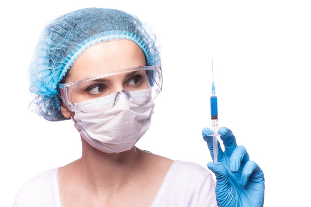 beautiful young girl in medical mask wearing glasses and gloves is holding a syringe with blue liquid - Photo, Image