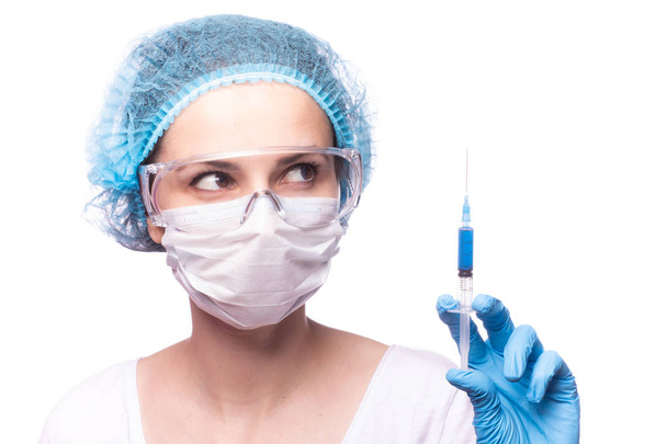 Tıp maskeli, gözlüklü ve eldivenli genç bir kız elinde mavi sıvı bir şırınga tutuyor. - Fotoğraf, Görsel