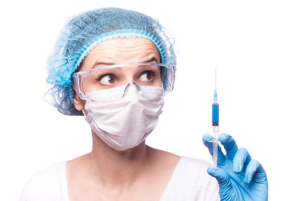 beautiful young girl in medical mask wearing glasses and gloves is holding a syringe with blue liquid - Fotoğraf, Görsel