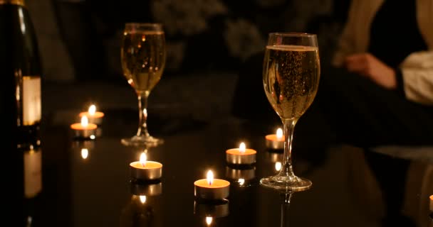 Glasses of champagne sparkling with nobody in background. On black glossy celebration table there is also red burning candles and bottle of sparkling wine. romantic valentine ambiance - Materiał filmowy, wideo