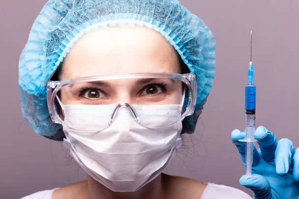 beautiful young girl in medical mask wearing glasses and gloves is holding a syringe with blue liquid - 写真・画像