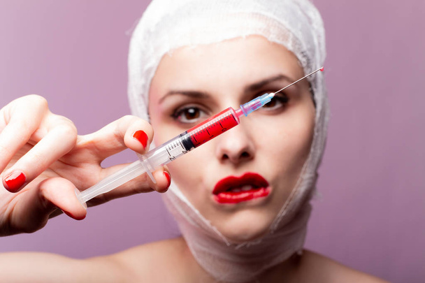 美しい少女赤い口紅で描かれた唇包帯で包まれた頭赤い液体の注射器の手の中に - 写真・画像