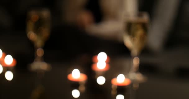 Women nervously waiting here date in background with glasses of sparkling champagne and red candles on glossy back table. Focus on left wine glass - Filmagem, Vídeo