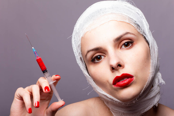 美しい少女赤い口紅で描かれた唇包帯で包まれた頭赤い液体の注射器の手の中に - 写真・画像