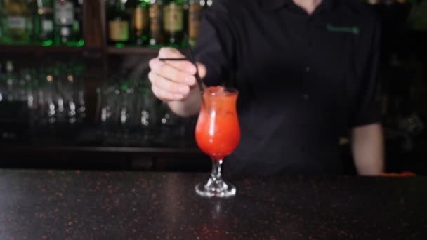 Mężczyzna barman serwujący napój klientowi. Zwolnij trochę. Tapster prezentuje i przynosi gotowy koktajl dla zwiedzających, przesuwając szkło do przodu do kamery nad stołem baru. Strzał w hd - Materiał filmowy, wideo