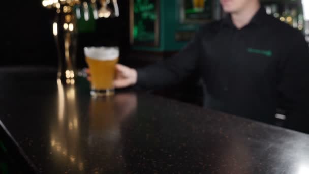 Tapster no balcão do bar segurando uma caneca de cerveja e apresentando-a ao cliente. Fecha. Barman rolando um copo de cerveja amarela ao longo da mesa preta. Movimento lento. hd
 - Filmagem, Vídeo