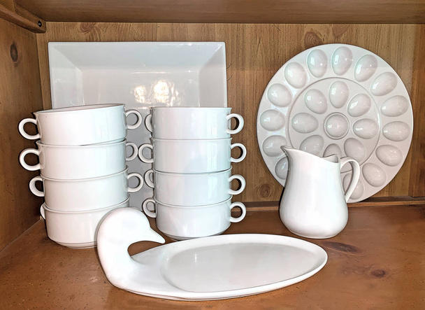Witte porseleinen schotels op open hutch 's plank in de keuken. Gestapelde soepkommen, dienblad, romier en eierschaal. - Foto, afbeelding