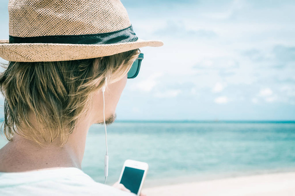 Side view of a young man with headphones listening to music on sea background - Valokuva, kuva