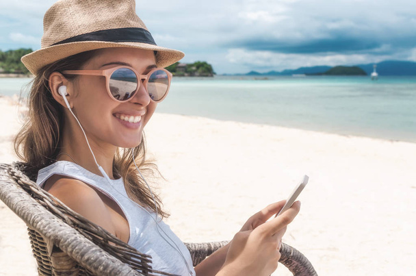 Young woman walking on beautiful bay using phone and headphones for communicate with friends and listening music - Foto, Imagen