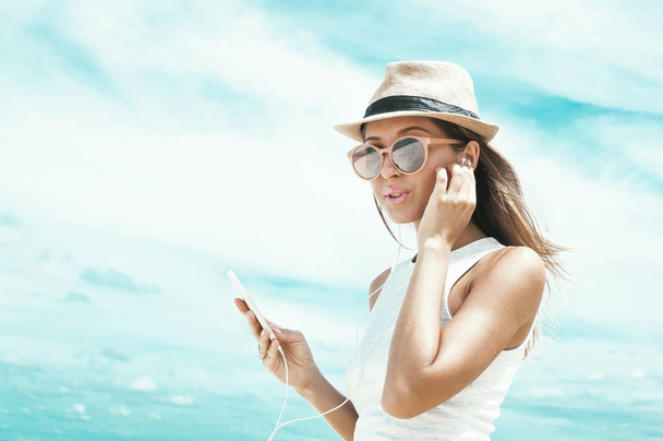 Young woman walking on beautiful bay using phone and headphones for communicate with friends and listening music - Photo, Image