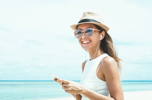 Mujer joven caminando por la hermosa bahía utilizando el teléfono y los auriculares para comunicarse con amigos y escuchar música
 - Foto, Imagen