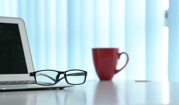 Office table with notebook laptop, eading glasses and coffee mug - Photo, image