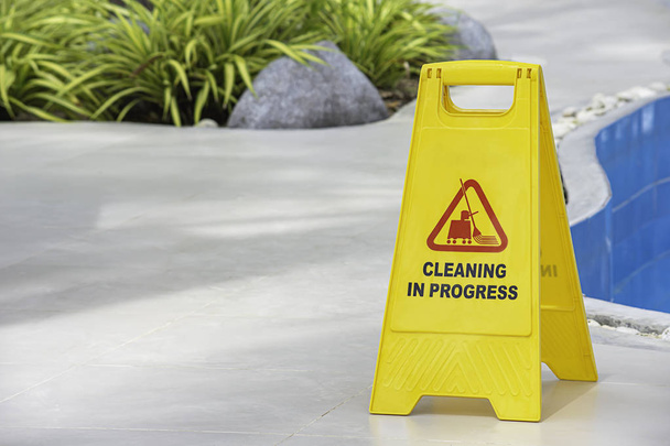 Trwa czyszczenie tablic ostrzegawczych obok basenu z żółtego tworzywa sztucznego. - Zdjęcie, obraz