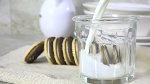 Pouring milk into a glass next to cream filled sandwich cookies - Materiał filmowy, wideo
