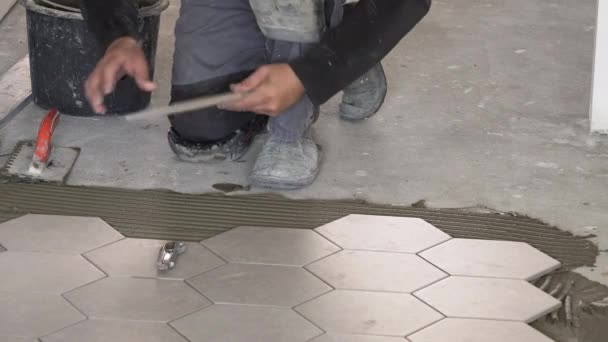 worker laying hexagon stone mass tiles on floor. - Video