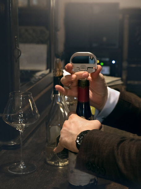 Ο σομελιέ ανοίγει ένα μπουκάλι κόκκινο κρασί αντίκα.  - Φωτογραφία, εικόνα