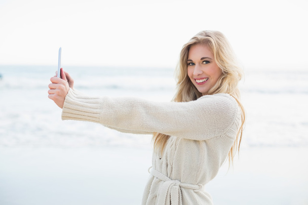Delighted blonde woman in wool cardigan taking a picture of herself with a tablet pc - Фото, зображення