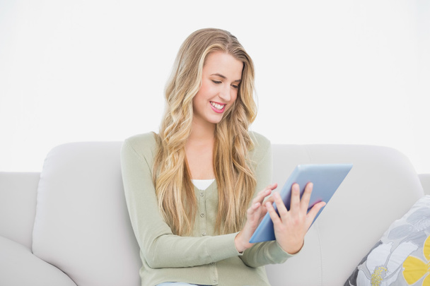 Happy pretty blonde using her tablet sitting on cosy sofa - 写真・画像