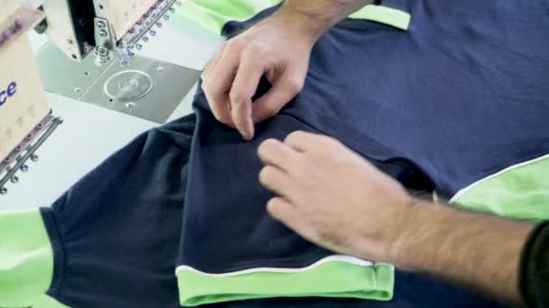 Mężczyzna w fabryce szycia sprawdza szycie koszulki - Materiał filmowy, wideo