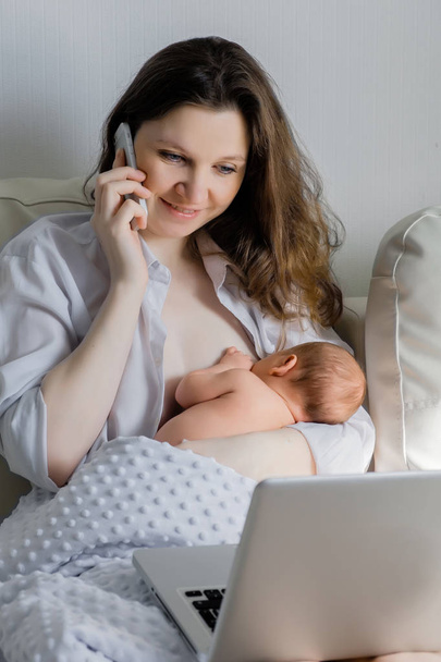 Cheerful young beautiful mother works as a freelancer at home, does remote work, breastfeeds her little child and reads information on a laptop. - Фото, зображення