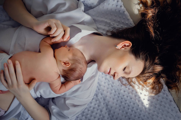 A newborn baby boy is lying on mom's chest. In a bright room. In the sun - Zdjęcie, obraz