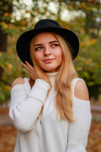 Autumn girl portraits. Model in a white sweater. Black hat. Yell - Photo, Image