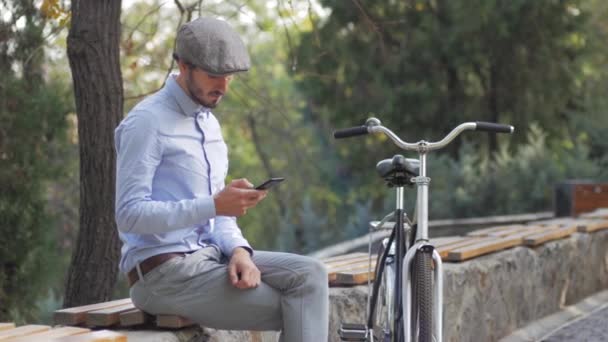 Young stylish male with retro bicycle riding on the streets in sunny day, portrait modern businessman with cellphone - Footage, Video
