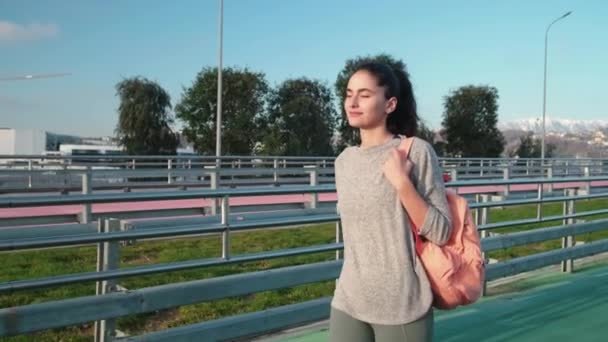 Smiling young brunette with backpack walking outside - Metraje, vídeo