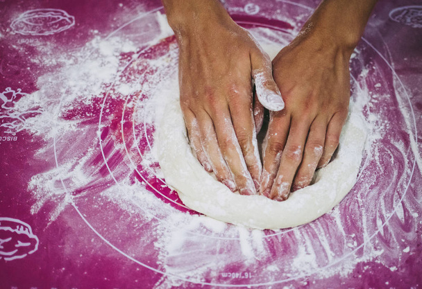Pizzaiolo kneedt pizza deeg met zijn handen, paarse achtergrond. Zelfgemaakt pizza bereidingsproces - Foto, afbeelding