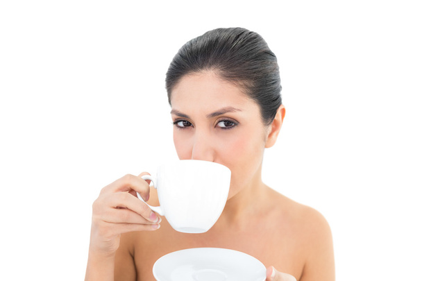 Pretty brunette holding a cup and saucer and taking a sip - Фото, зображення