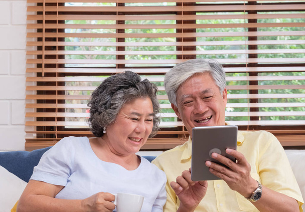 Asian senior couple using table compute and drink coffee sitting at sofa in living room at home.senior with technology lfiestyle.aging at home concept. - Fotó, kép