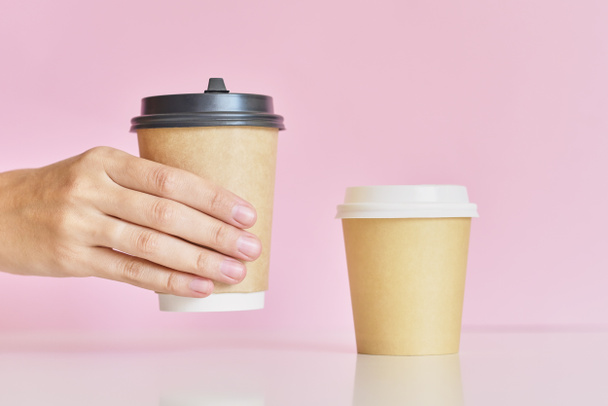 Kobieta ręka wziąć na dwóch filiżanki papieru do kawy na różowym tle - Zdjęcie, obraz
