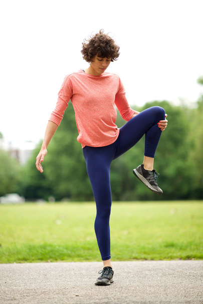 Полный портрет активной женщины, растягивающей мышцы в парке, стоящей на одной ноге
 - Фото, изображение