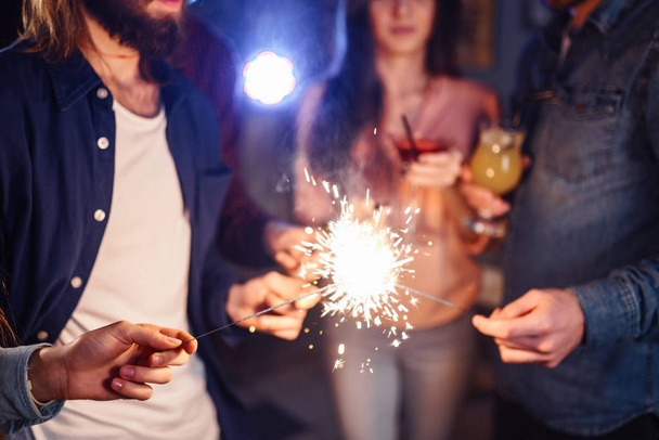 Group of happy people holding sparklers at party and smiling.Young people celebrating New Year together. Friends lit sparklers. Friends enjoying with sparklers in evening. Blur Background. - 写真・画像