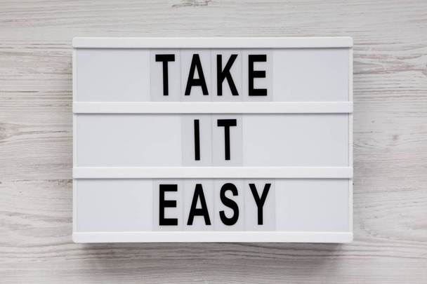 "Πάρτε εύκολο" λέξεις σε ένα lightbox σε μια λευκή ξύλινη επιφάνεια, να - Φωτογραφία, εικόνα