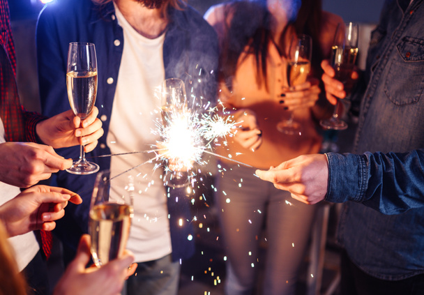 Group of happy people holding sparklers at party and smiling.Young people celebrating New Year together. Friends lit sparklers. Friends enjoying with sparklers in evening. Blur Background. - Photo, Image