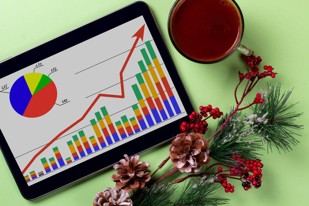 A tablet with a business graph on the desktop. Christmas decorations. - Foto, Imagen