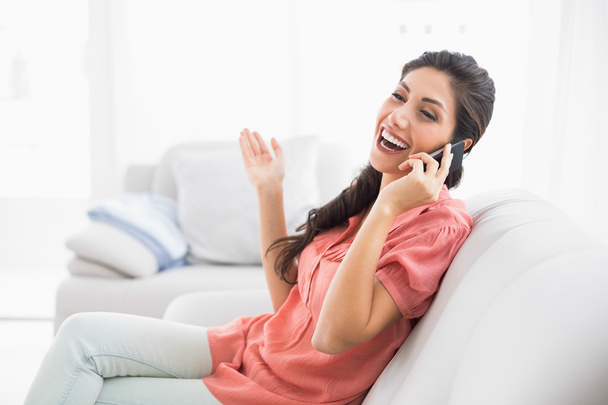 Laughing brunette sitting on her sofa on the phone - Zdjęcie, obraz