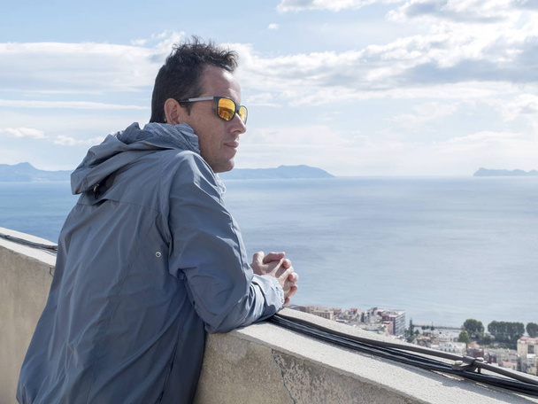 Primo piano uomo in giacca blu appoggiato su ringhiera recinzione guardando lontano verso il mare a Napoli, Italia
 - Foto, immagini