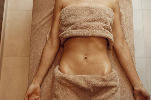 Slim woman in towel lying on massage table, top view. Massaging and relaxation, body and skin care. Female person relaxing in spa salon - Photo, Image